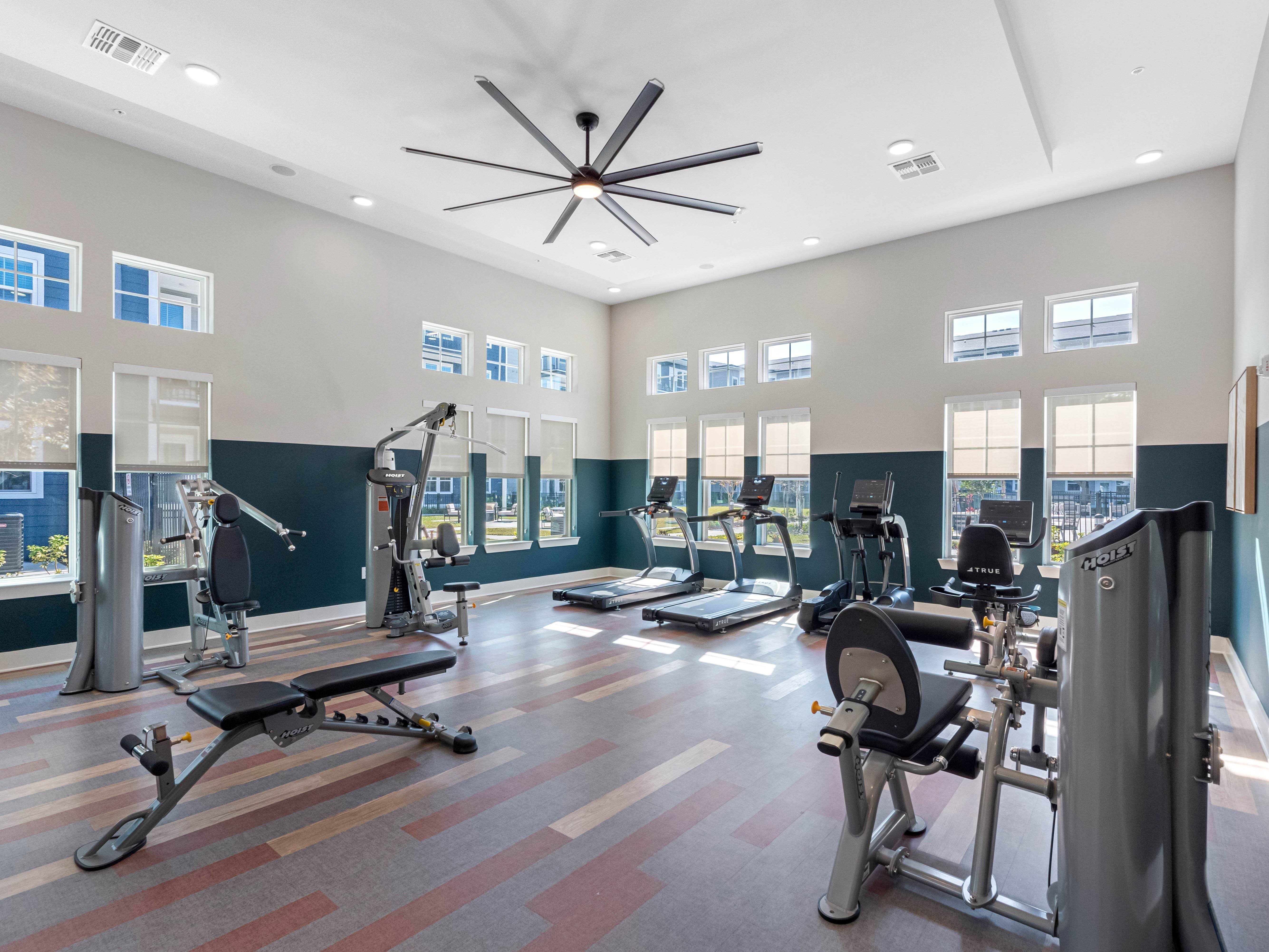 A gym with a variety of equipment including treadmills, weights, and a ceiling fan.